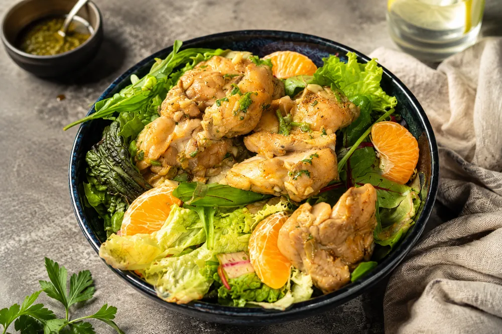 Greek lemon chicken salad — sliced chicken over mixed greens with orange segments in a blue bowl