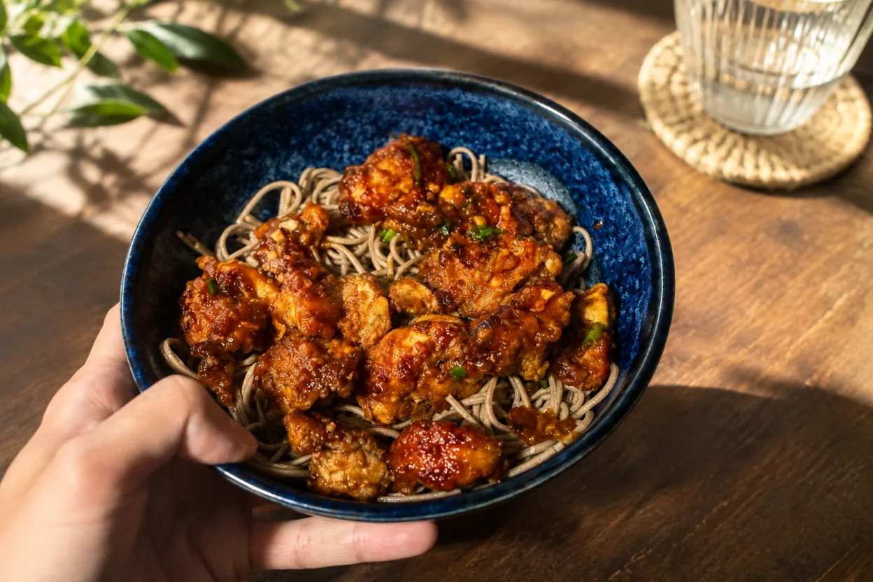 Sweet and spicy honey sriracha chicken — crispy glazed chicken pieces piled over sesame soba noodles in a bowl